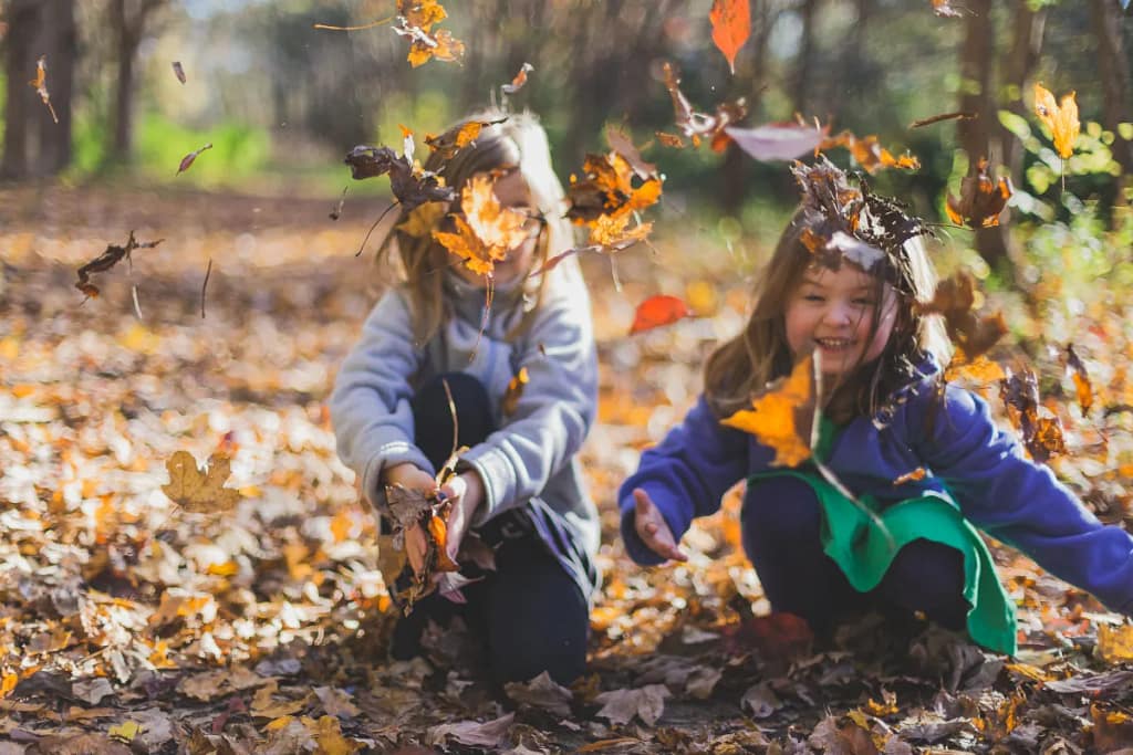 two girls playing in the fallen leaves, finding joy in God's creation. 