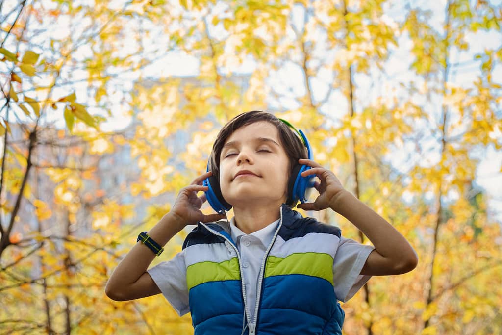 A young boy is feeling the fruit of the spirit Peace while closing his eyes and wearing noise cancelling headphones in the forest.