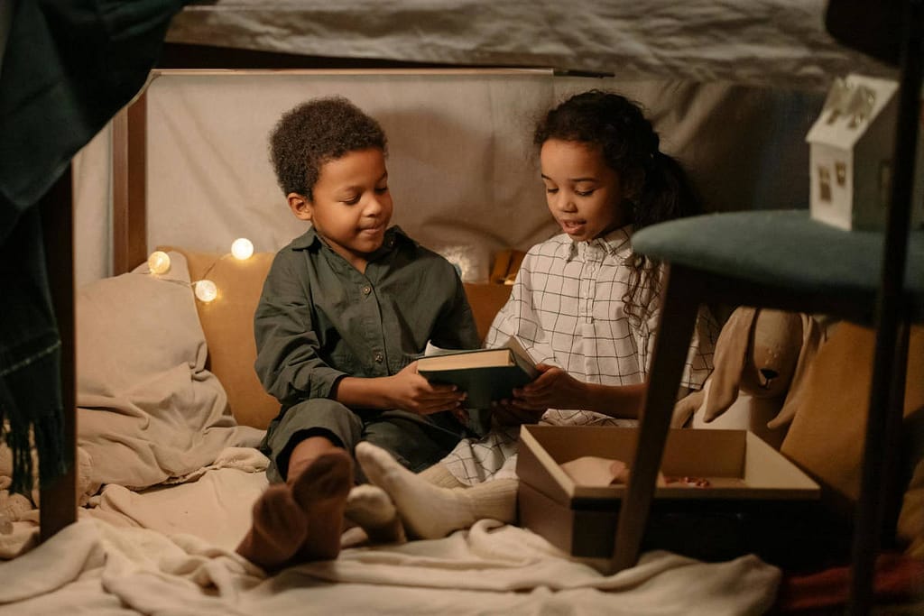 Two siblings reading a book together in a fort, demonstrating the fruit of the Spirit Kindness towards each other.