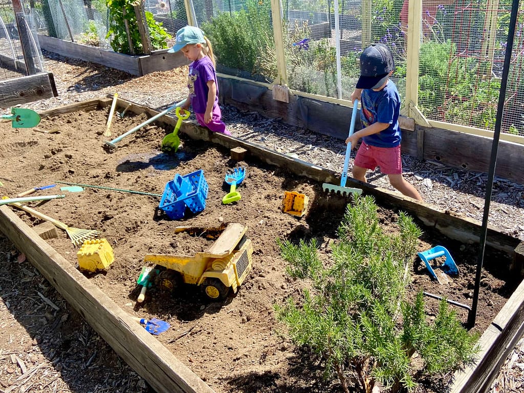 a boy and a girl digging in a planter box of dirt