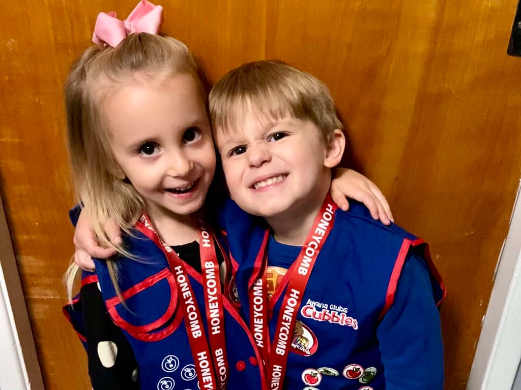 a boy and a girl wearing their awana cubby vests with their end of the year awana medals