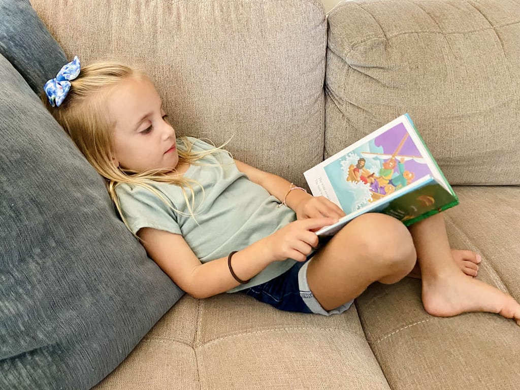 a girl laying on a couch, reading a child bible