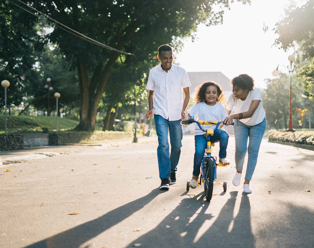 A young girl is feeling the Fruit of the Spirit Peace while her parents are helping her learn to ride a tricycle.