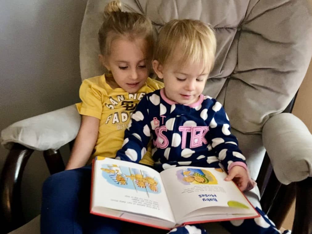 Two siblings sitting together on a rocking chair, reading a toddler Bible, learning about the Fruit of the Spirit Peace.